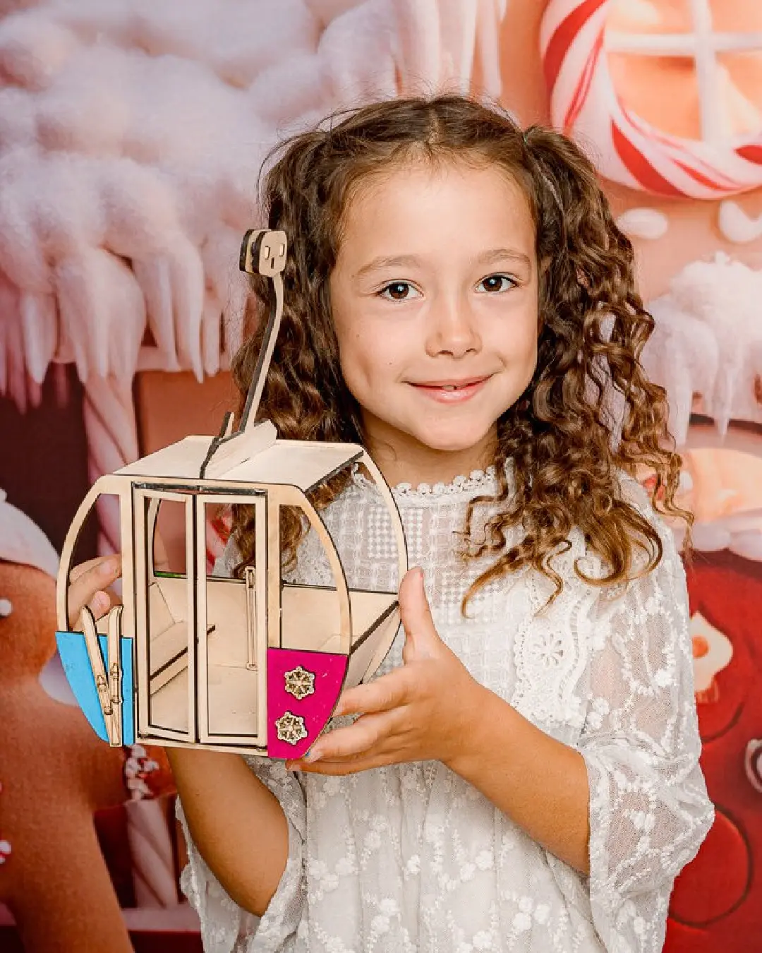 Une petite fille qui tient fièrement sa télécabine en bois décoré avec de la peinture et des éléments en bois (flocons, skis, étoiles.) Ateliers de création en bois pour les familles dans les stations de ski et les offices de tourisme. Les enfants et les familles fabriquent une télécabine en bois composée de 20 pièces en bois. Cette animation convient aux offices de tourisme est accessibles aux enfants dès 6 ans et leurs familles ! Cet événement proposé par Les graines d'Eveil est accessible avec et sans inscription aux enfants à partir de 6 ans et leurs familles. Ils décorent et assemblent leurs création. Ils repartent avec une télécabine gravés avec le nom de l'événement ou de la station de ski. Cette animation est à destination des stations de Savoie et offices de tourisme (Courchevel, Tignes, Val d'Isère, Sainte Foy, La Rosière, Les Arcs, Peisey-Vallandry, La Plagne, Val Thorens) et Haute Savoie (Megève, Combloux, Chamonix, Morzine les Gets, Annecy, Avoriaz, La Cluzaz...). Il le personnalise avec des mini-ski, des flocons, des étoiles, des sapins... Il utilise un fil en bois pour la suspendre à la maison. C'est un souvenir unique et inoubliable de leurs vacances en stations de ski.
